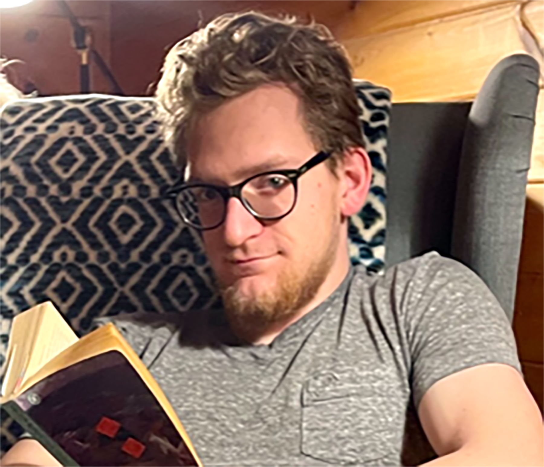 Ben looking at the camera while reading a book in a wingback chair.